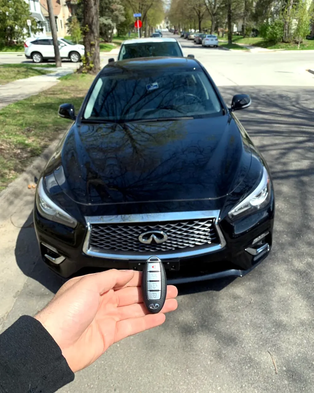 New Infiniti smart key held in front of an Infiniti Q50 on a residential street after a job in Franklin Square, NY
