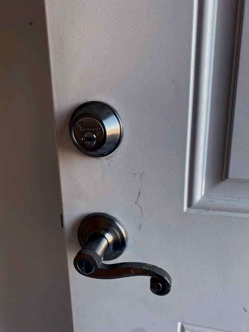 Deadbolt above a lever handle on a white apartment door