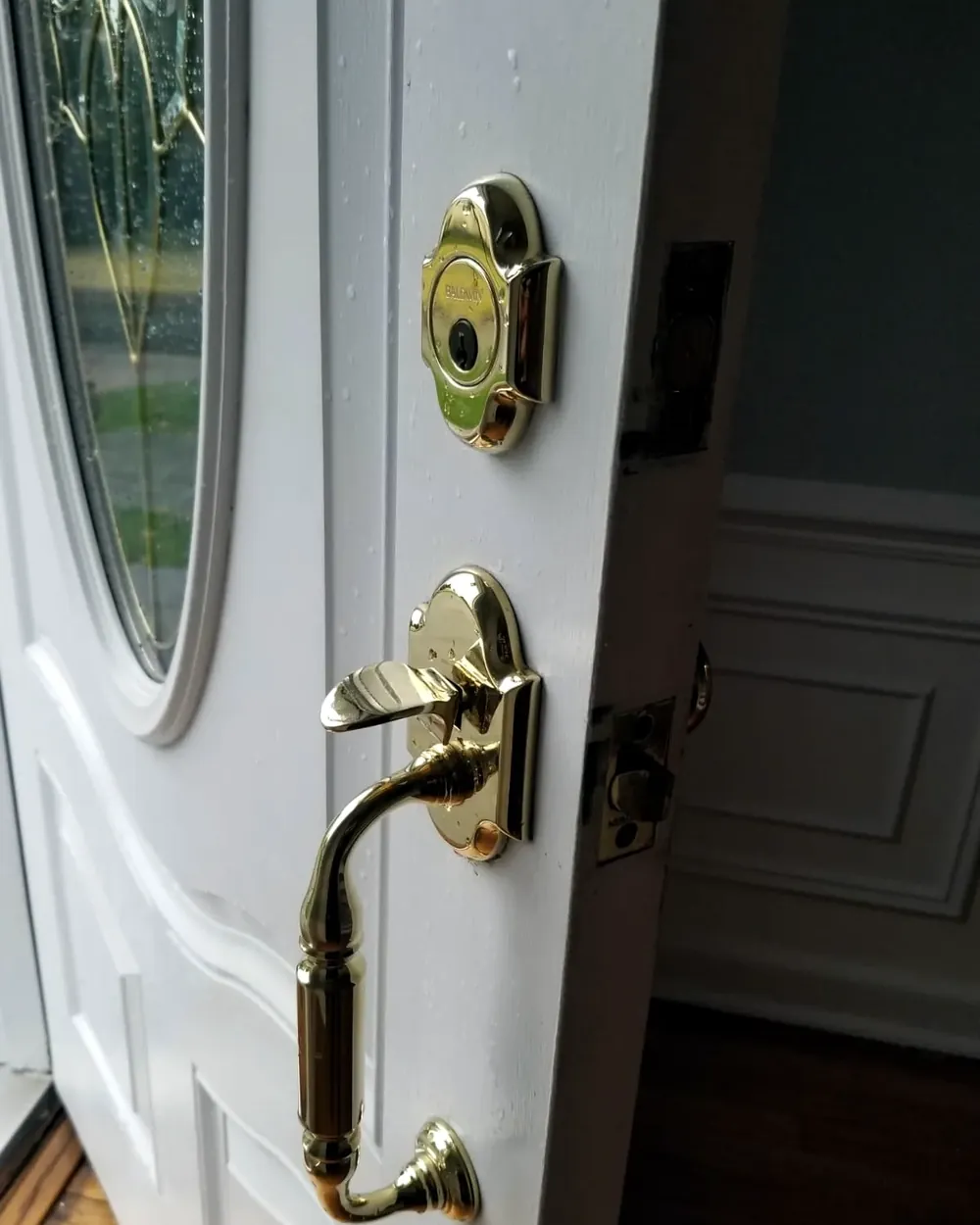 Brass handleset and deadbolt on a white front door with an oval glass window