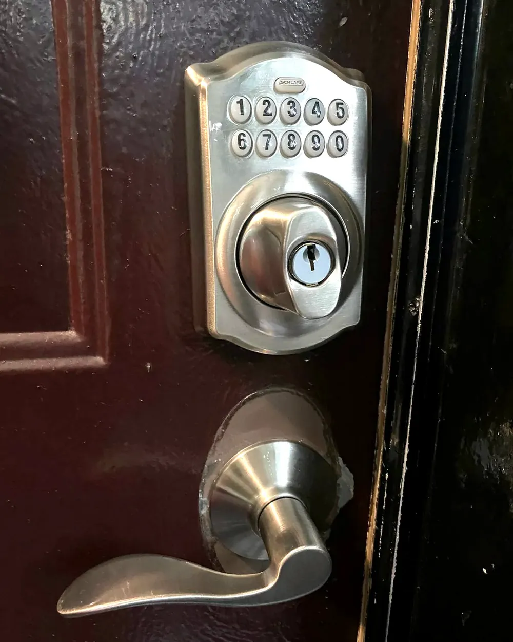 Keypad deadbolt above a lever handle on a dark front door