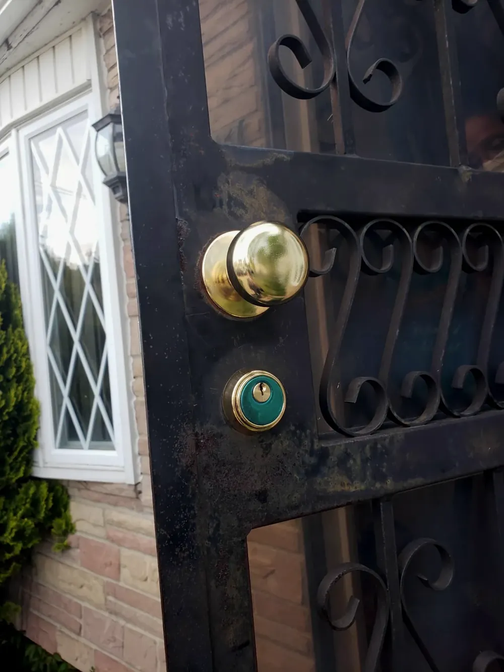 Brass knob and deadbolt on a black wrought-iron gate outside a brick house